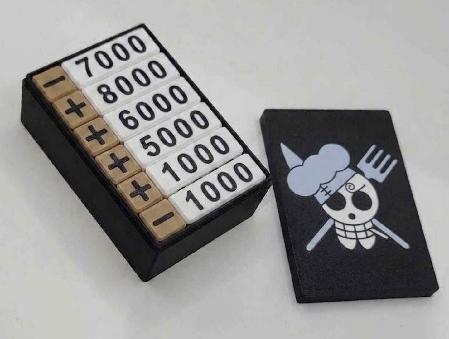 White and gold One Piece damage counters in a black box with a black Sanji skull lid