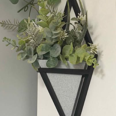 Black triangular wall planter holding green foliage